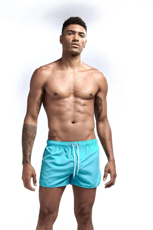 Man wearing blue short swim shorts with drawstring by Good Trouble Garments from GOOD TROUBLE FASHION