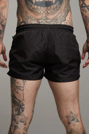 Black short sexy swim trunks by GOOD TROUBLE FASHION worn by tattooed male model from the back