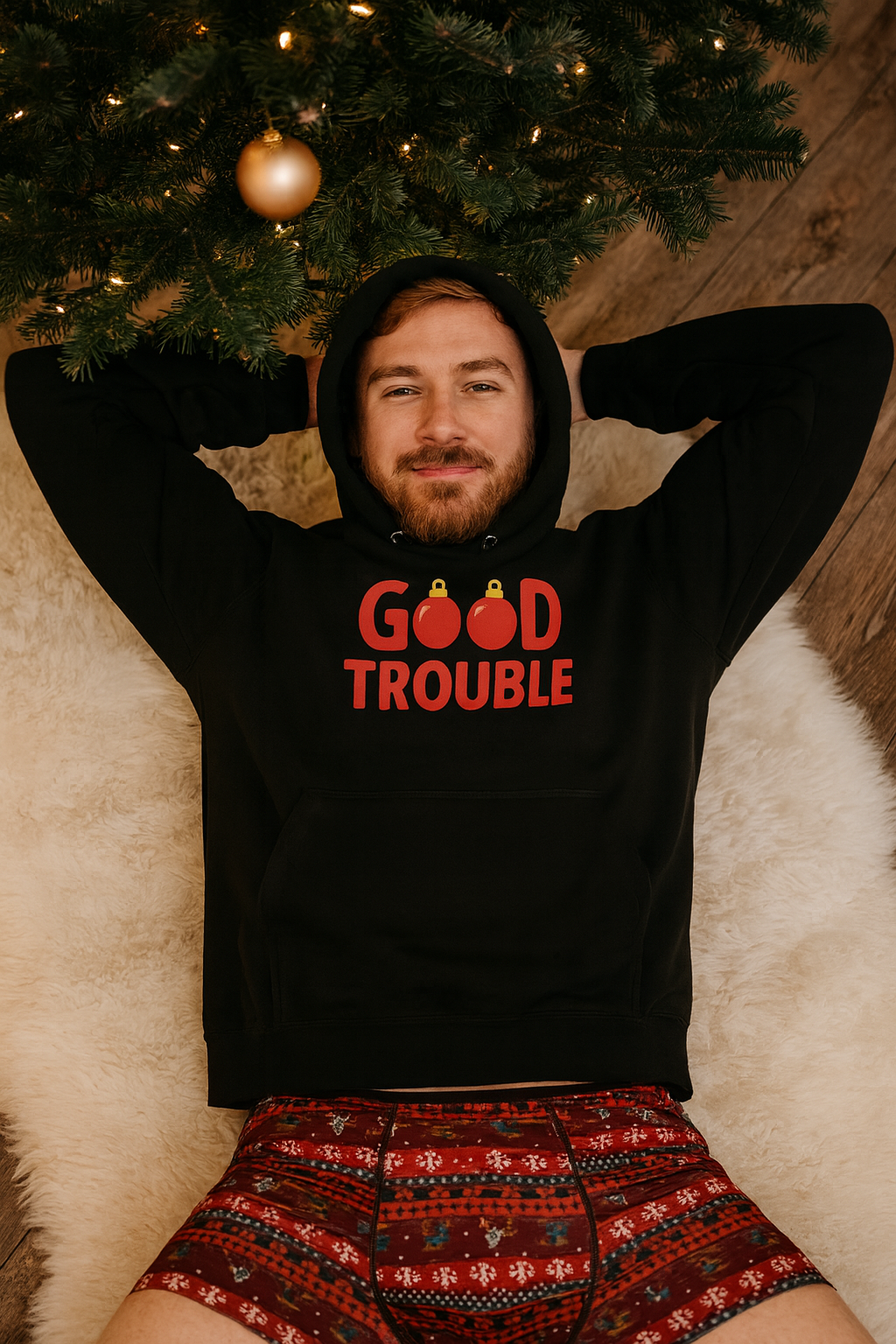 Man wearing Good Trouble holiday hoodie laid on a cozy rug under a Christmas tree