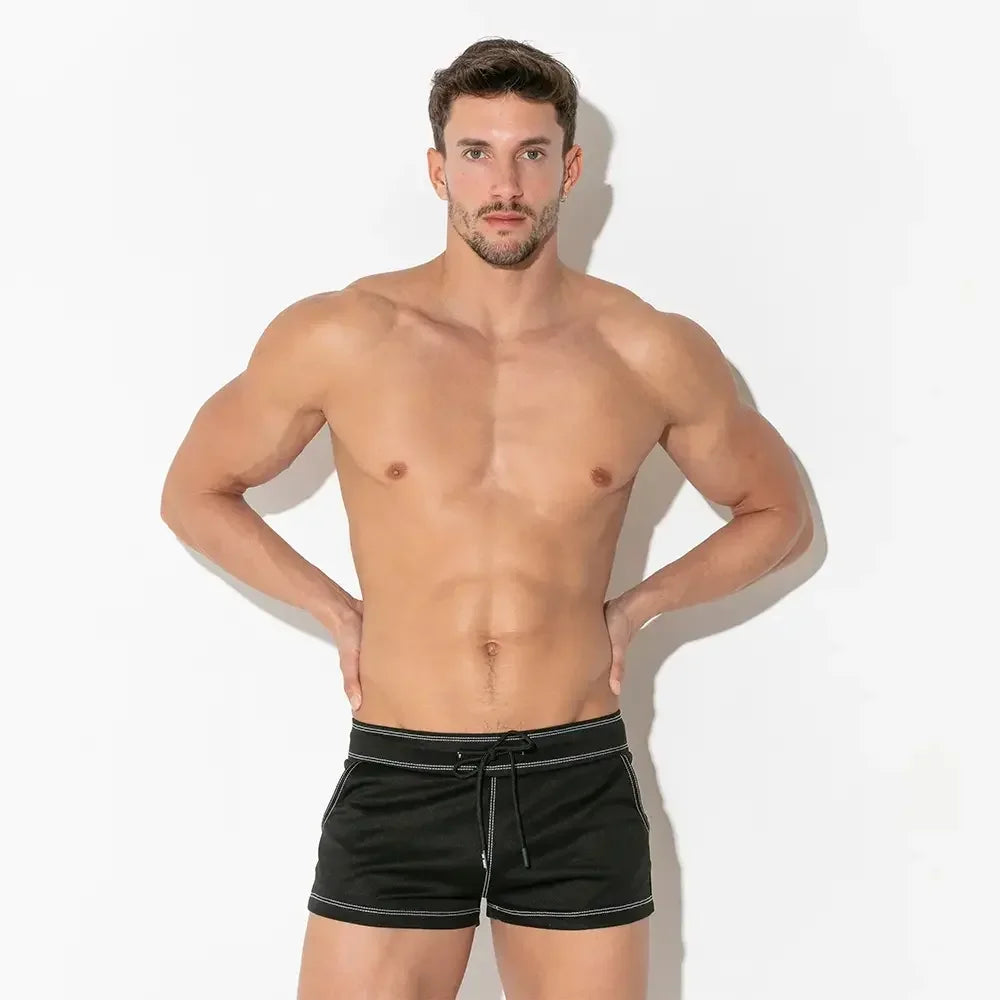 Good Trouble Garments short black swimwear for men by CODE 22 modeled by fit man on white background